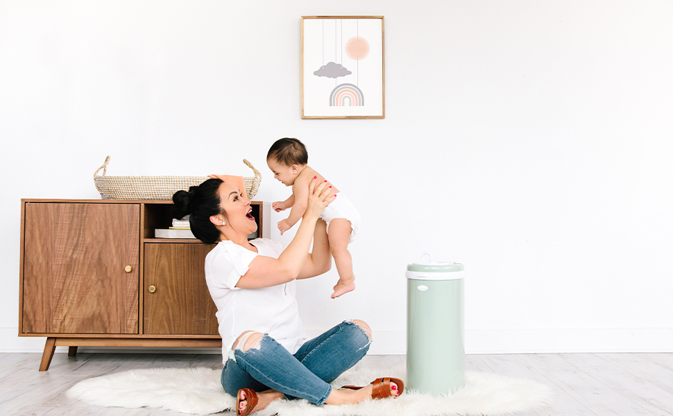 Madre sentada junto a la sabia cubeta de pañales Ubbi levantando y mirando al bebé